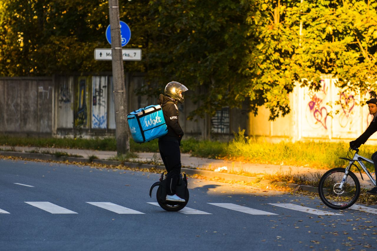 Delivery rider on electric unicycle crossing Riga street in evening light.